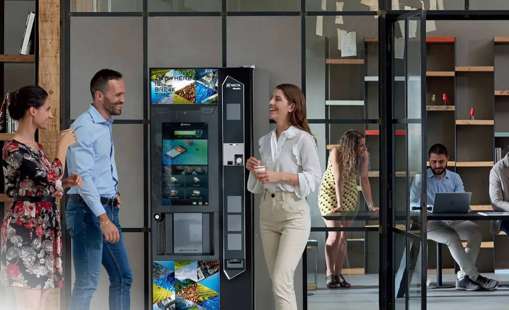 Collaborateurs autour d'un distributeur automatique à écran tactile dans des bureaux niçois
